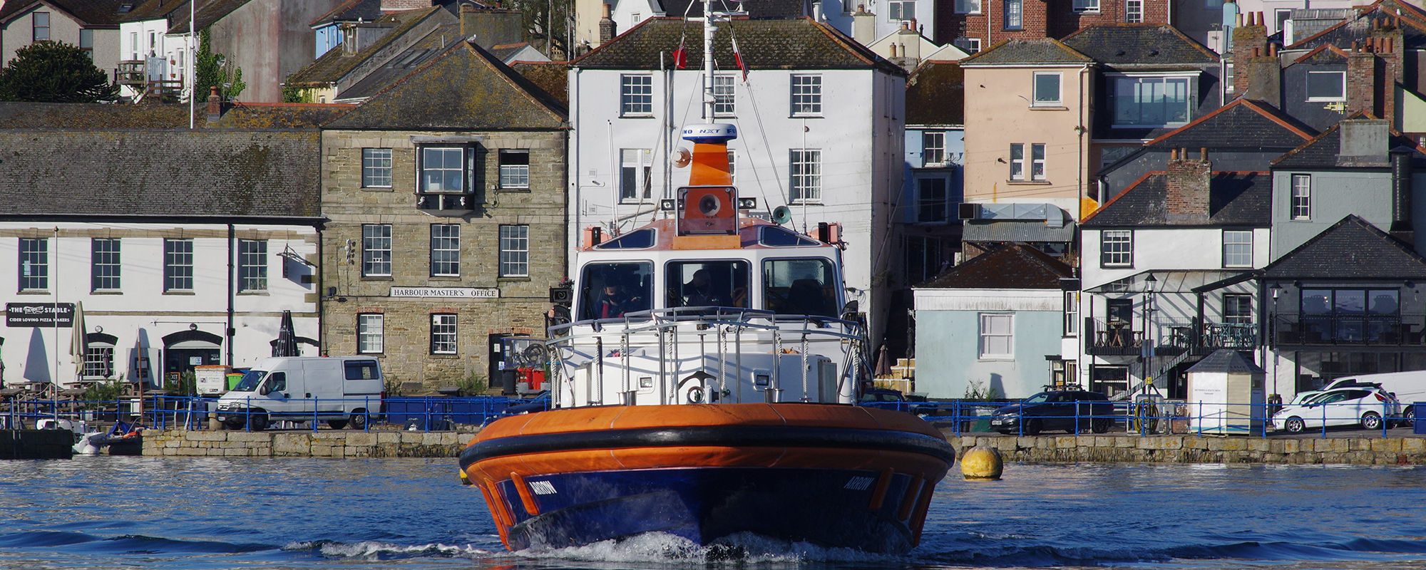 A pilot ship leaves Falmouth Harbour with the town visible in the background.